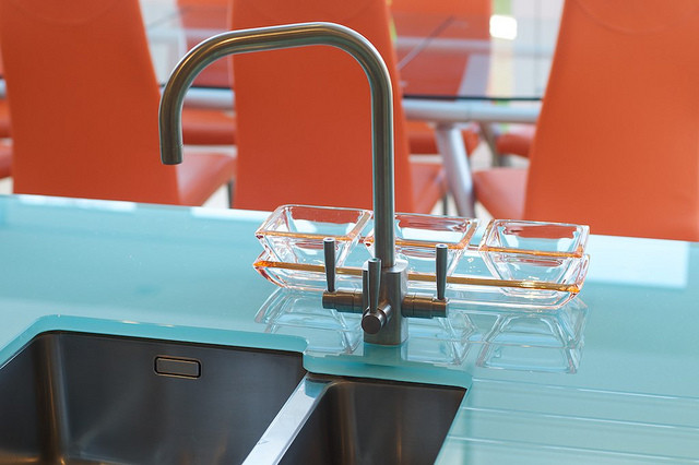 Immagine di una cucina abitabile design con lavello a vasca singola, top in vetro, elettrodomestici in acciaio inossidabile e nessuna isola