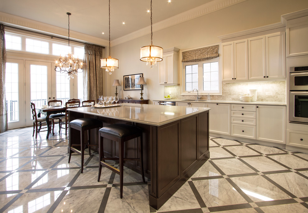 Photo of a large traditional u-shaped kitchen/diner in Detroit with a double-bowl sink, shaker cabinets, white cabinets, engineered stone countertops, beige splashback, travertine splashback, stainless steel appliances, marble flooring, an island and white floors.