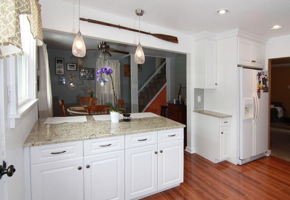 Lantlig inredning av ett mellanstort kök, med en rustik diskho, luckor med upphöjd panel, vita skåp, granitbänkskiva, grått stänkskydd, stänkskydd i keramik, rostfria vitvaror, mellanmörkt trägolv och en halv köksö