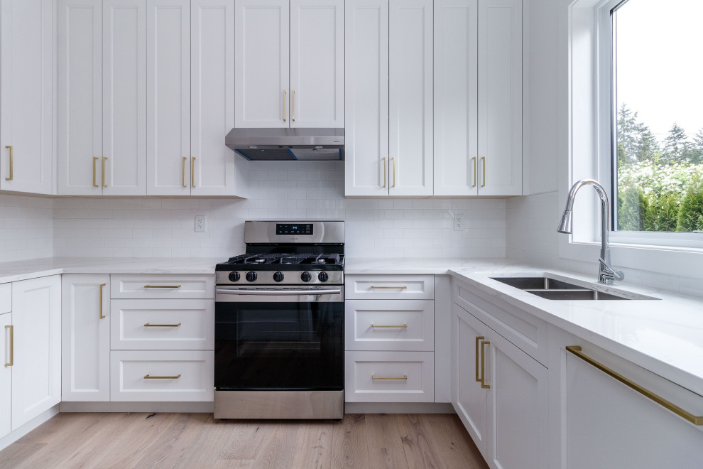 Inredning av ett klassiskt mellanstort vit vitt kök, med en undermonterad diskho, vita skåp, bänkskiva i kvarts, vitt stänkskydd, stänkskydd i keramik, rostfria vitvaror, ljust trägolv, beiget golv och luckor med infälld panel