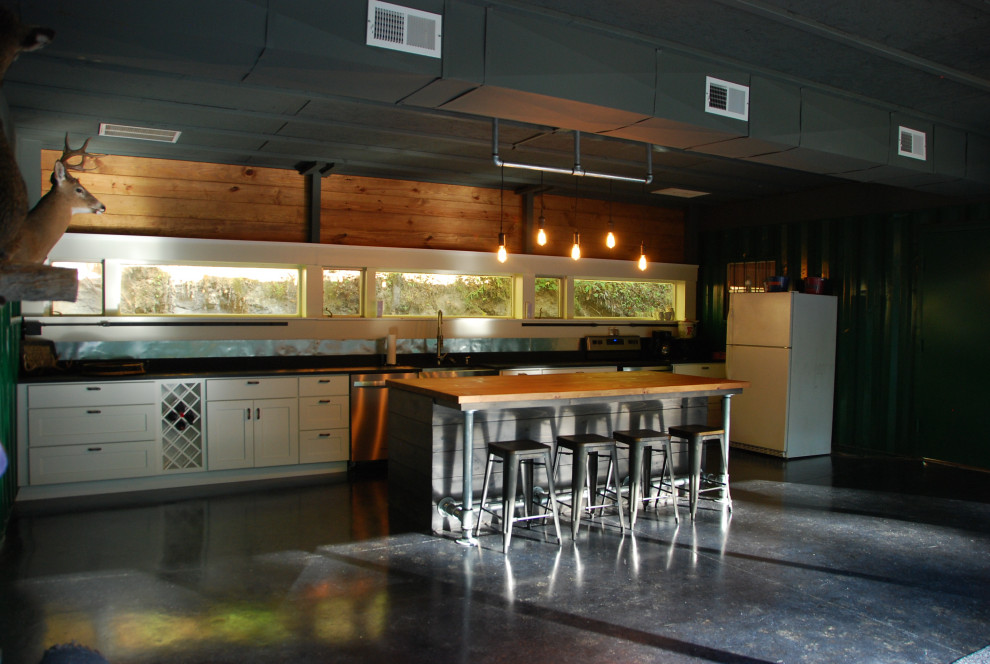 Exempel på ett mellanstort industriellt svart linjärt svart kök med öppen planlösning, med en rustik diskho, skåp i shakerstil, vita skåp, granitbänkskiva, stänkskydd med metallisk yta, rostfria vitvaror, betonggolv, en köksö och grått golv