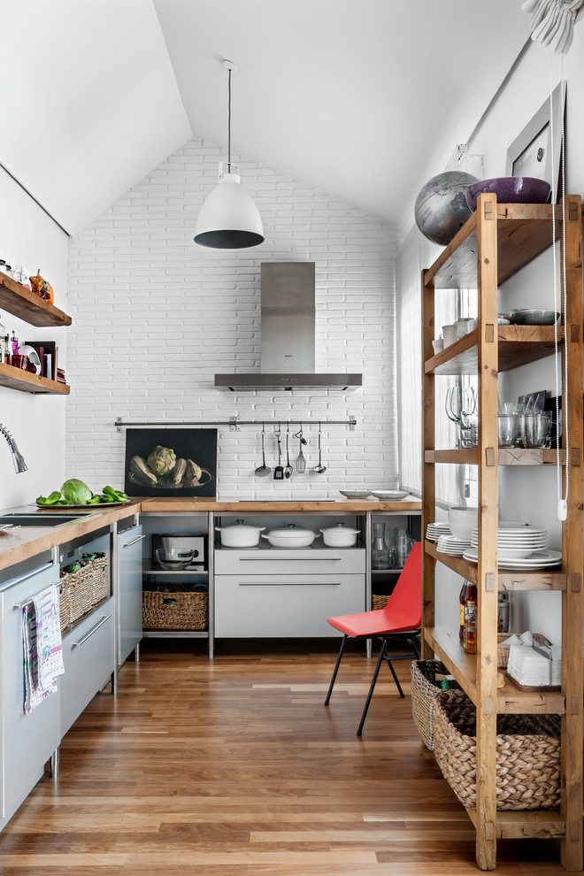 Foto de cocinas en L urbana de tamaño medio cerrada sin isla con armarios con paneles lisos, suelo de madera en tonos medios, encimera de madera, puertas de armario grises, salpicadero blanco, salpicadero de azulejos tipo metro y electrodomésticos de acero inoxidable