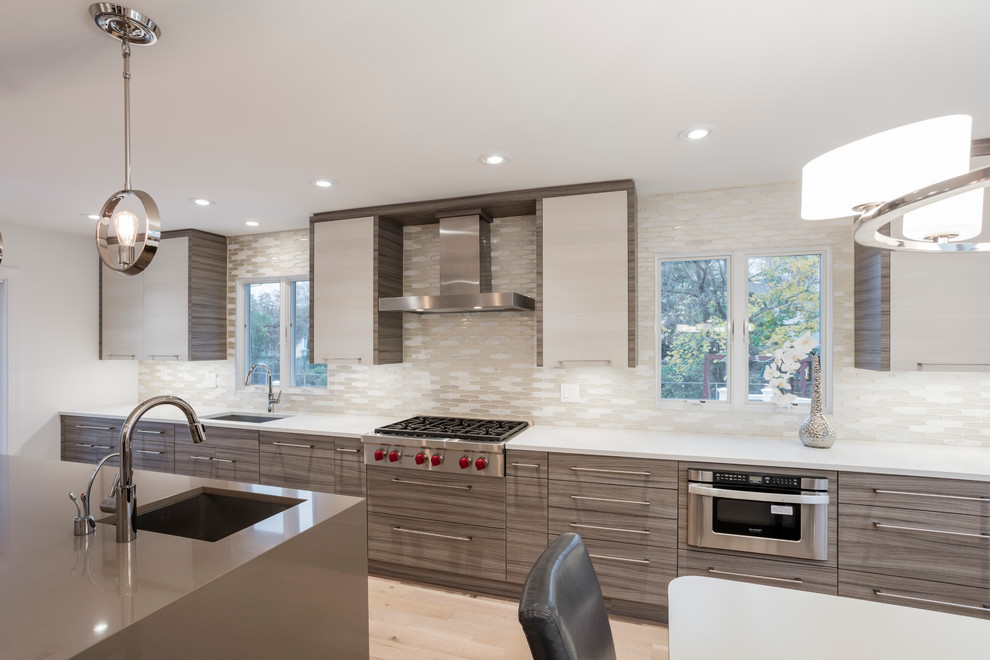 Design ideas for a medium sized contemporary single-wall kitchen/diner in New York with a built-in sink, flat-panel cabinets, grey cabinets, engineered stone countertops, integrated appliances, an island, beige splashback, glass tiled splashback and light hardwood flooring.