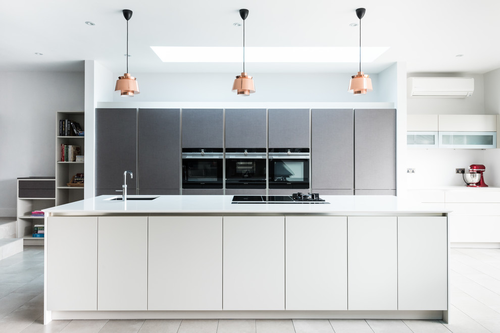 Diseño de cocina gris y blanca moderna con fregadero bajoencimera, armarios con paneles lisos, puertas de armario grises, electrodomésticos negros, una isla y suelo gris