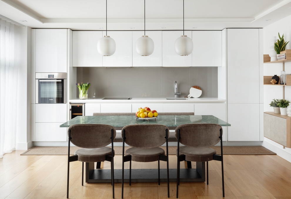Inspiration for a contemporary single-wall kitchen/diner in London with a submerged sink, flat-panel cabinets, white cabinets, grey splashback, glass sheet splashback, stainless steel appliances, light hardwood flooring, no island, beige floors and white worktops.