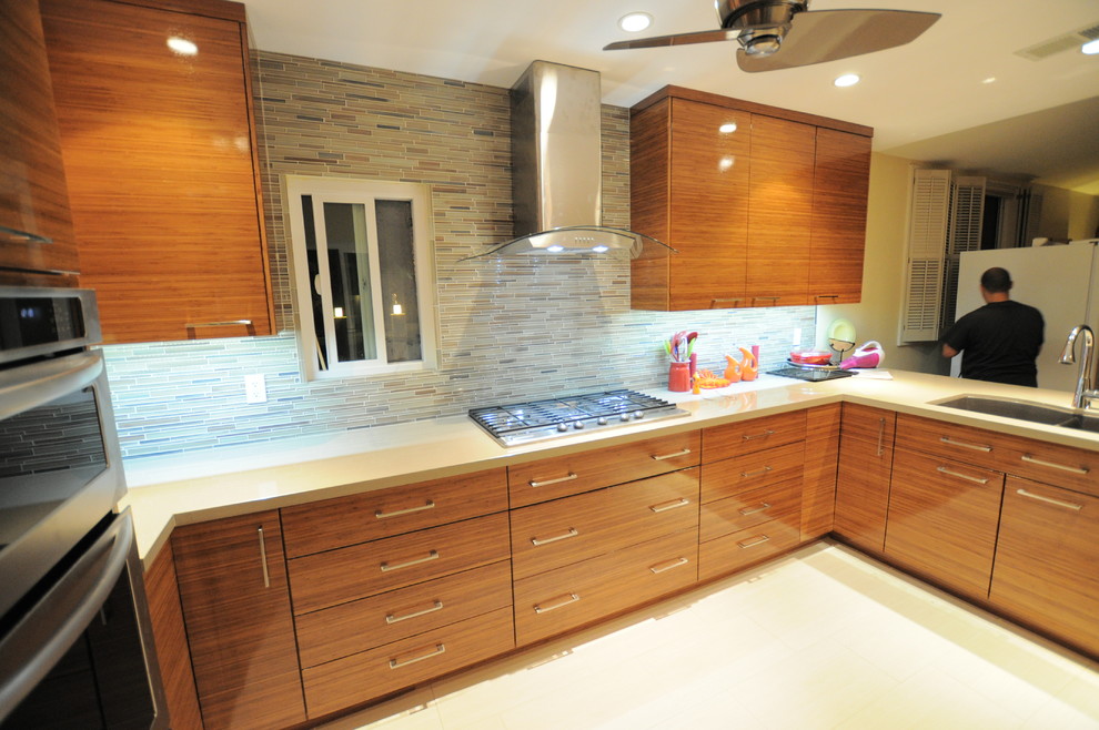 Example of a trendy u-shaped eat-in kitchen design in Los Angeles with a double-bowl sink, flat-panel cabinets, medium tone wood cabinets, quartz countertops, multicolored backsplash, glass tile backsplash and stainless steel appliances