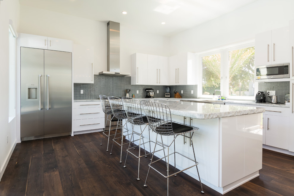 Moderne Küche in L-Form mit flächenbündigen Schrankfronten, weißen Schränken, Küchenrückwand in Grau, Rückwand aus Mosaikfliesen, Küchengeräten aus Edelstahl, dunklem Holzboden und Kücheninsel in Jacksonville