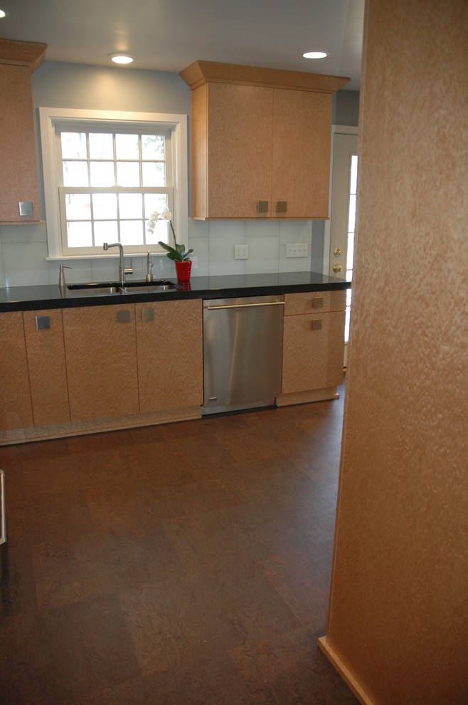 Foto på ett mellanstort funkis kök, med en undermonterad diskho, släta luckor, skåp i ljust trä, granitbänkskiva, vitt stänkskydd, stänkskydd i glaskakel, rostfria vitvaror och korkgolv
