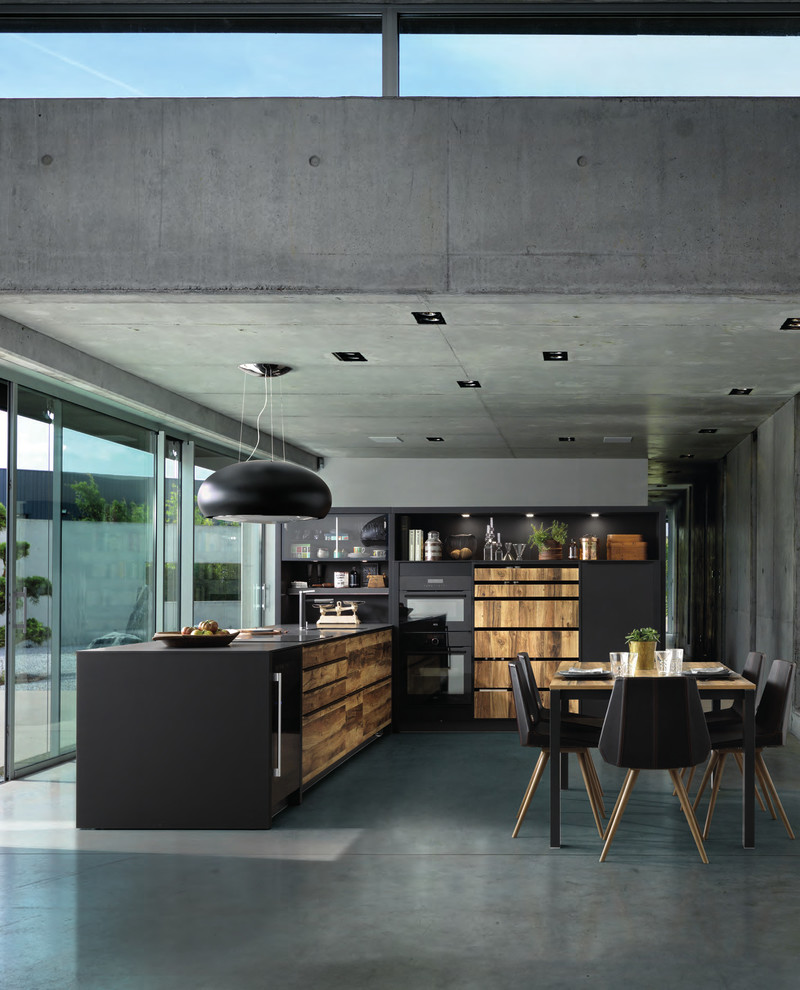 Foto på ett mellanstort funkis kök, med svarta skåp, bänkskiva i kvarts, svarta vitvaror, betonggolv, grått golv, en undermonterad diskho, släta luckor, grått stänkskydd och en halv köksö