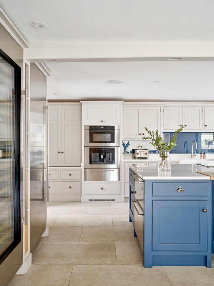 Inredning av ett modernt stort vit vitt kök, med en rustik diskho, skåp i shakerstil, blå skåp, bänkskiva i kvartsit, blått stänkskydd, glaspanel som stänkskydd, rostfria vitvaror, kalkstensgolv, en köksö och beiget golv