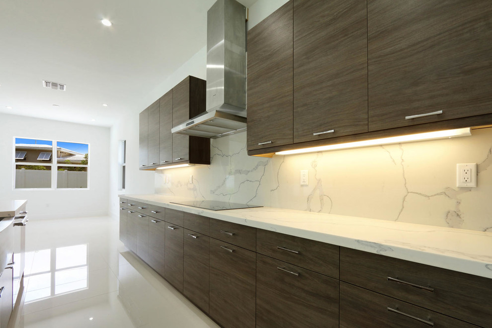 This is an example of an expansive contemporary l-shaped open plan kitchen in Miami with a belfast sink, flat-panel cabinets, brown cabinets, engineered stone countertops, white splashback, stone slab splashback, stainless steel appliances, porcelain flooring, an island and beige floors.
