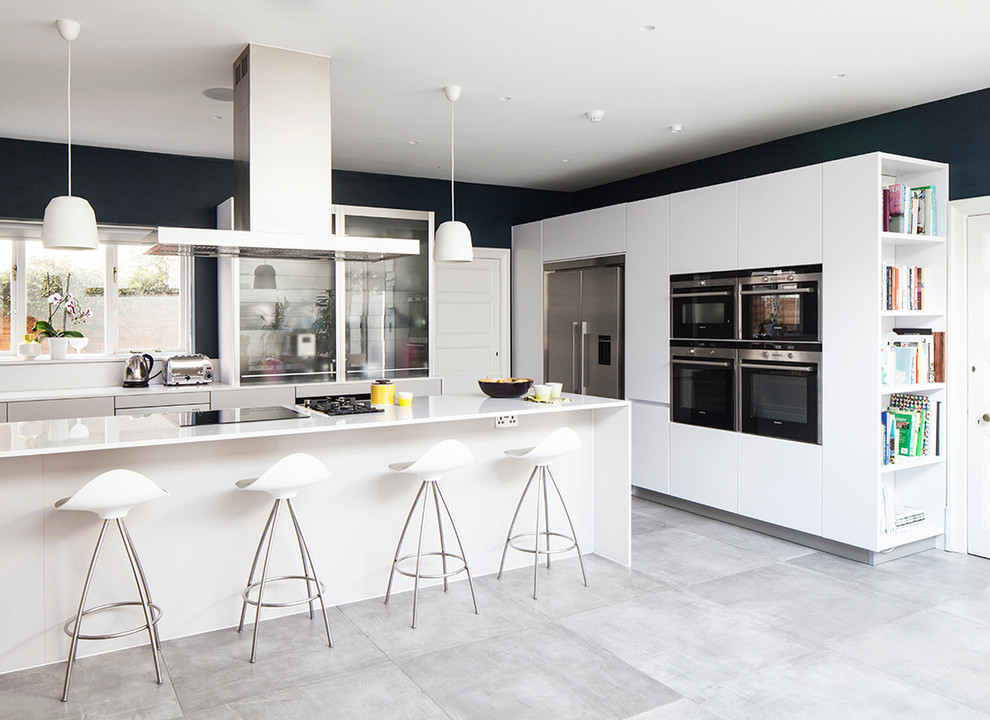 Design ideas for a large contemporary u-shaped open plan kitchen in Sussex with a built-in sink, flat-panel cabinets, white cabinets, glass sheet splashback, white appliances, concrete flooring, an island, laminate countertops and white splashback.