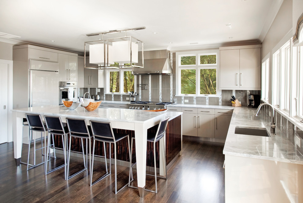 Inspiration for a large contemporary u-shaped dark wood floor and brown floor kitchen remodel in Charleston with a single-bowl sink, flat-panel cabinets, gray cabinets, gray backsplash, paneled appliances, granite countertops, glass tile backsplash, two islands and white countertops