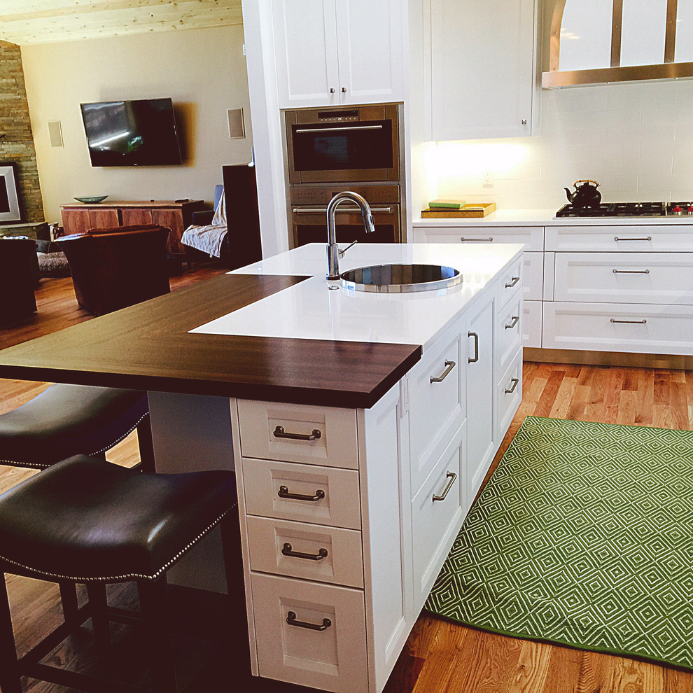 Mittelgroße Moderne Wohnküche mit Waschbecken, Lamellenschränken, weißen Schränken, Arbeitsplatte aus Holz, Küchenrückwand in Weiß, Rückwand aus Glasfliesen, Küchengeräten aus Edelstahl, braunem Holzboden und Kücheninsel in Albuquerque