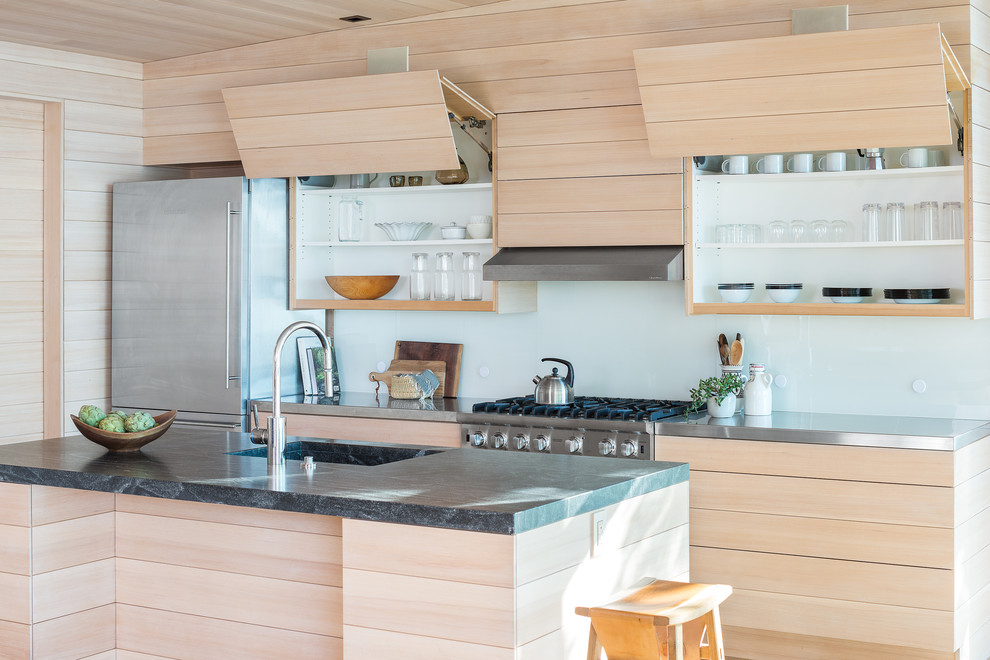 Bild på ett rustikt kök, med skåp i ljust trä, bänkskiva i rostfritt stål, vitt stänkskydd, glaspanel som stänkskydd, rostfria vitvaror, en köksö och en enkel diskho
