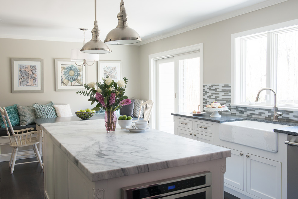 Photo of a classic u-shaped open plan kitchen in New York with recessed-panel cabinets, white cabinets, composite countertops, multi-coloured splashback, matchstick tiled splashback, dark hardwood flooring, an island, a belfast sink and stainless steel appliances.