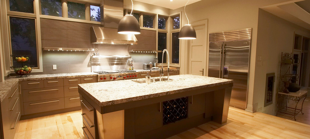 Modern inredning av ett mellanstort kök, med en nedsänkt diskho, släta luckor, skåp i ljust trä, granitbänkskiva, grått stänkskydd, rostfria vitvaror, ljust trägolv och en köksö