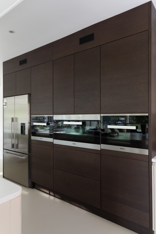 Cette image montre une cuisine ouverte design avec un placard à porte plane, des portes de placard marrons, un électroménager noir et îlot.