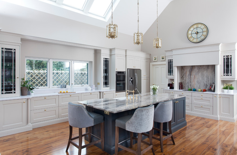 Design ideas for a classic l-shaped kitchen in Other with a belfast sink, shaker cabinets, grey cabinets, grey splashback, stainless steel appliances, medium hardwood flooring, an island, brown floors and white worktops.
