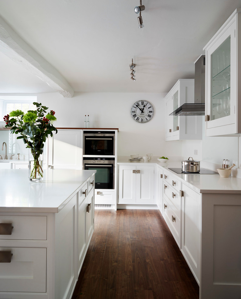 Foto på ett mellanstort funkis kök och matrum, med skåp i shakerstil, vita skåp, bänkskiva i kvartsit, en köksö, en undermonterad diskho, vitt stänkskydd, glaspanel som stänkskydd, svarta vitvaror och mörkt trägolv