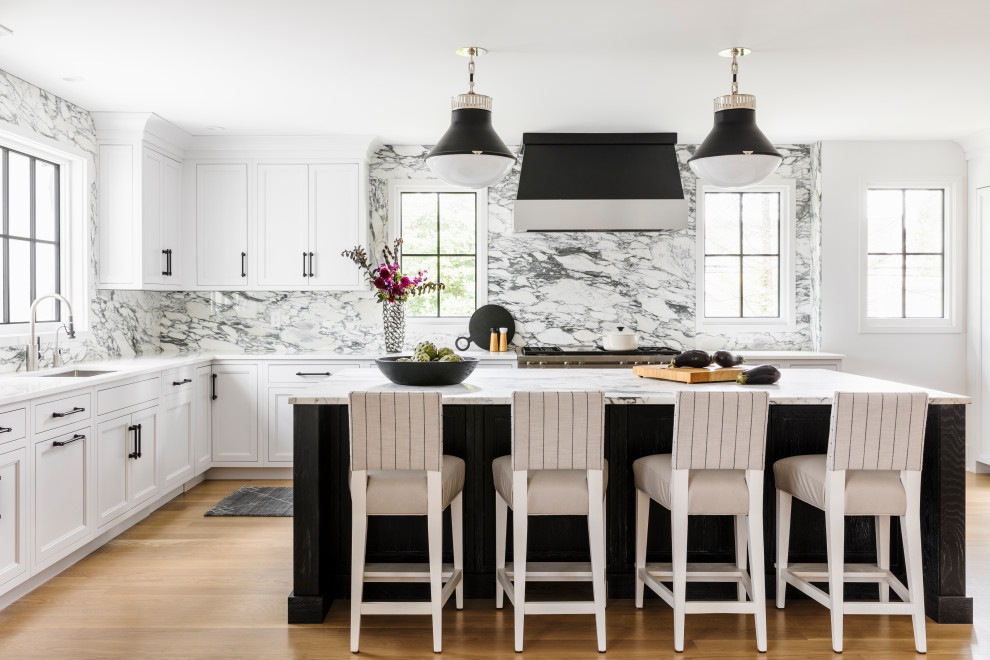 Bild på ett funkis vit vitt l-kök, med en undermonterad diskho, luckor med infälld panel, vita skåp, vitt stänkskydd, stänkskydd i sten, rostfria vitvaror, mellanmörkt trägolv, en köksö och brunt golv