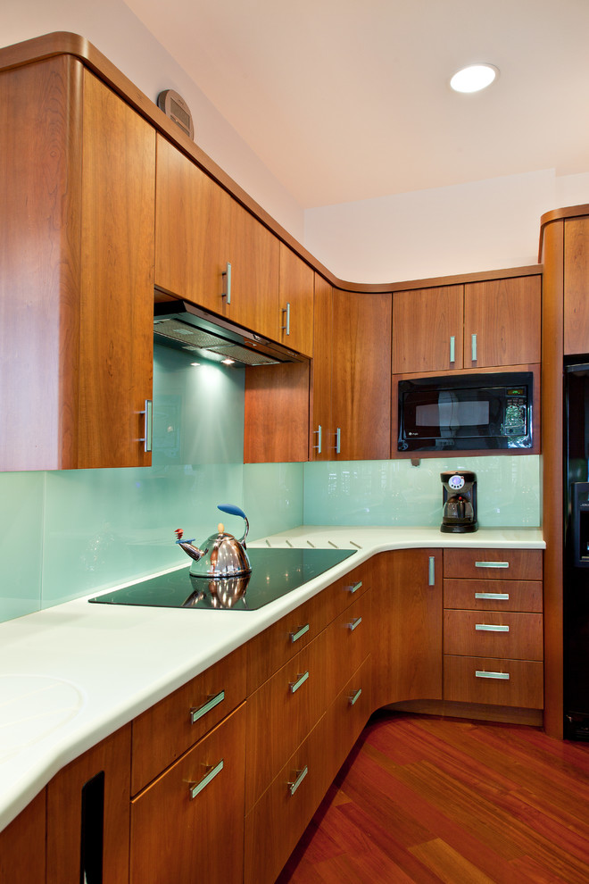 Modelo de cocina contemporánea con armarios con paneles lisos, puertas de armario de madera oscura, salpicadero de vidrio templado y electrodomésticos negros