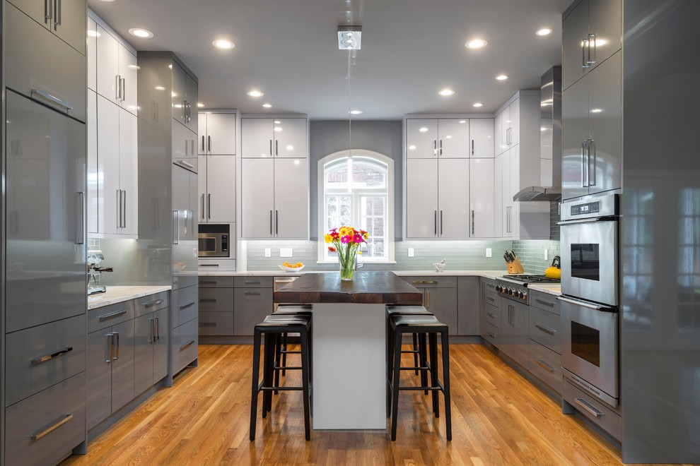 Klassische Küche mit flächenbündigen Schrankfronten, grauen Schränken, Rückwand aus Glasfliesen, Küchengeräten aus Edelstahl, braunem Holzboden und Kücheninsel in St. Louis