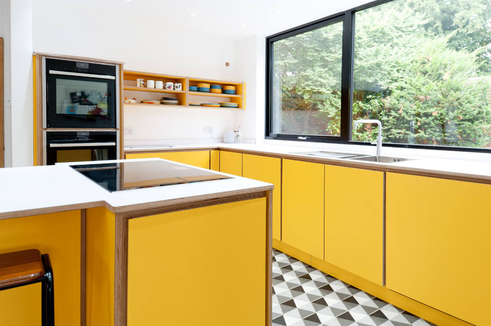 На фото: угловая кухня среднего размера в современном стиле с обеденным столом, плоскими фасадами, желтыми фасадами, столешницей из ламината, островом, разноцветным полом и белой столешницей с