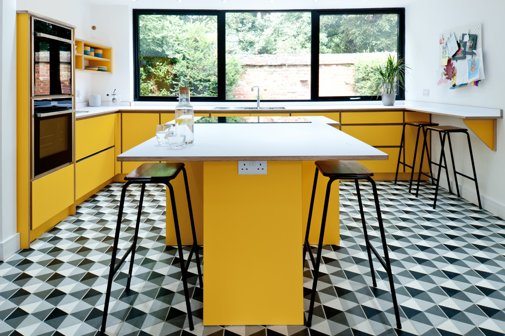 Идея дизайна: угловая кухня среднего размера в современном стиле с обеденным столом, плоскими фасадами, желтыми фасадами, столешницей из ламината, островом, белой столешницей, двойной мойкой, техникой из нержавеющей стали, разноцветным полом, красивой плиткой и мойкой у окна