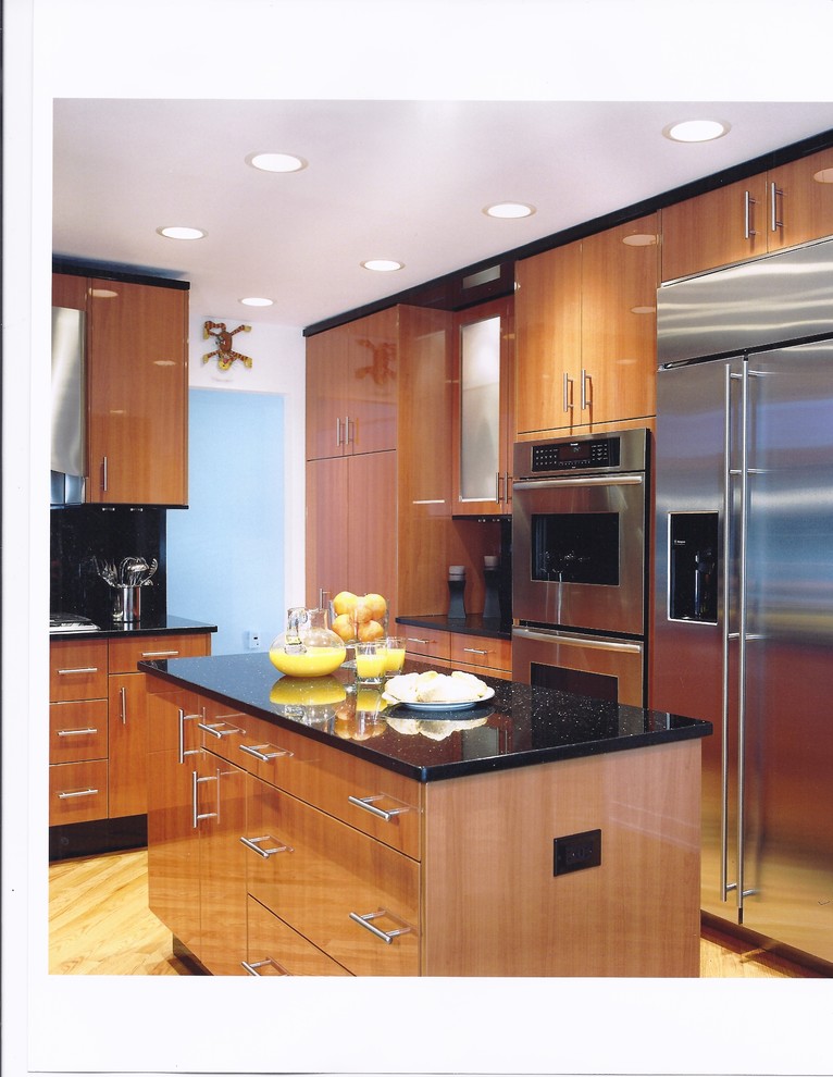 Modern inredning av ett avskilt, litet u-kök, med en undermonterad diskho, släta luckor, skåp i mellenmörkt trä, granitbänkskiva, svart stänkskydd, stänkskydd i sten, rostfria vitvaror och ljust trägolv
