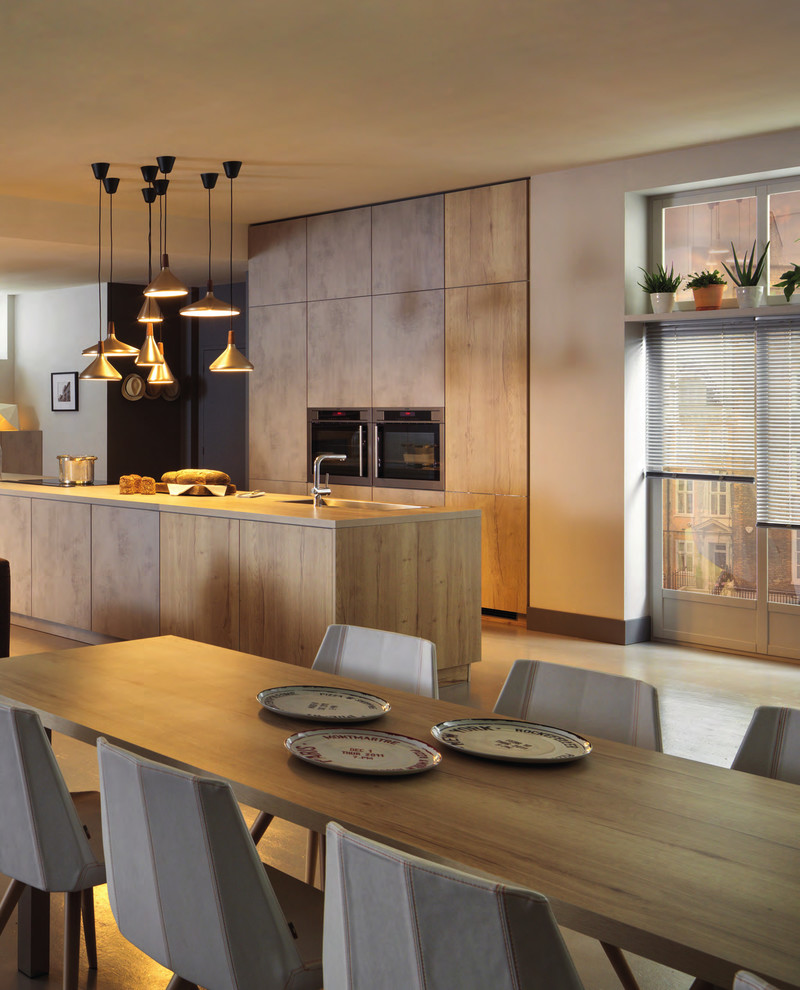 Свежая идея для дизайна: большая прямая кухня-гостиная в современном стиле с плоскими фасадами, светлыми деревянными фасадами, столешницей из ламината, черной техникой, бетонным полом, островом и серым полом - отличное фото интерьера