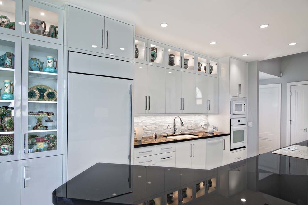 Foto på ett stort funkis linjärt kök med öppen planlösning, med en undermonterad diskho, släta luckor, vita skåp, bänkskiva i kvarts, grått stänkskydd, stänkskydd i stickkakel, integrerade vitvaror, betonggolv och en köksö