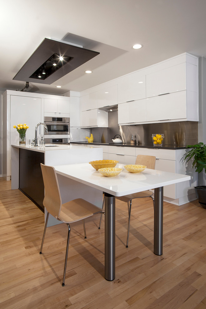 Moderne Wohnküche in L-Form mit flächenbündigen Schrankfronten, weißen Schränken, Küchenrückwand in Metallic, braunem Holzboden und Kücheninsel in Detroit