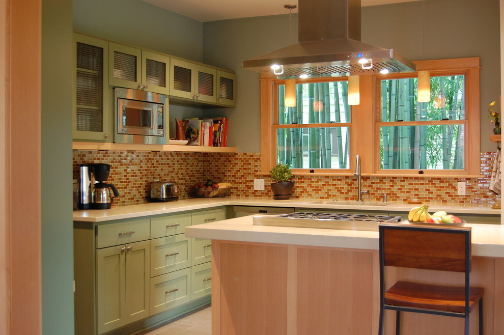 Idéer för ett amerikanskt kök, med stänkskydd i mosaik, rostfria vitvaror, gröna skåp, orange stänkskydd, luckor med glaspanel, bänkskiva i kvarts och en köksö
