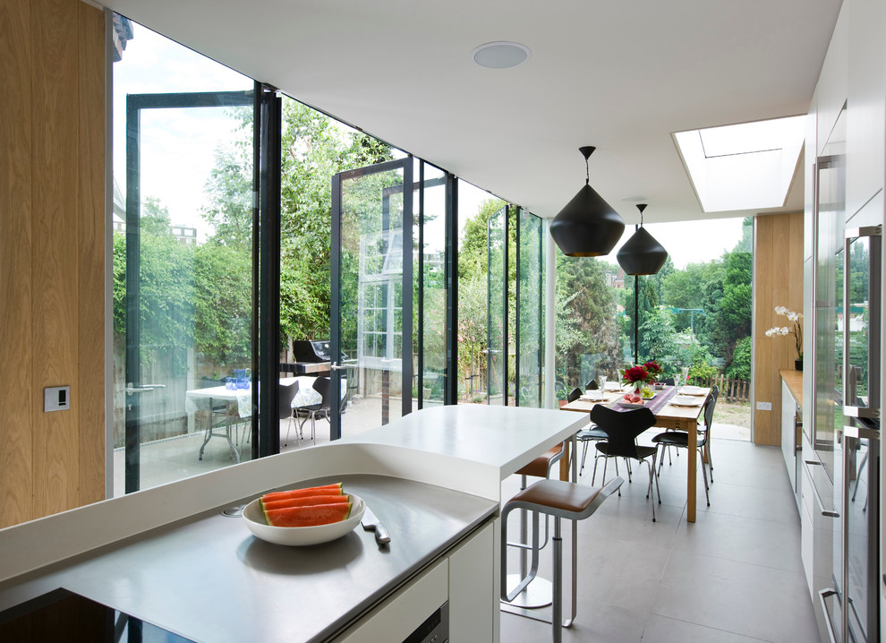 Diseño de cocina comedor lineal contemporánea de tamaño medio con fregadero bajoencimera, armarios con paneles lisos, puertas de armario blancas, encimera de acero inoxidable, electrodomésticos de acero inoxidable, suelo de baldosas de cerámica y una isla