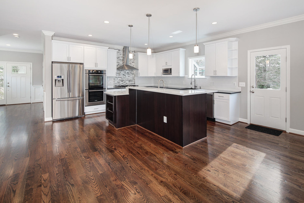 Inspiration for a transitional l-shaped dark wood floor open concept kitchen remodel in DC Metro with recessed-panel cabinets, white cabinets, solid surface countertops, multicolored backsplash, glass tile backsplash, stainless steel appliances, an island and an undermount sink