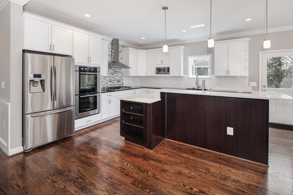 Transitional l-shaped dark wood floor open concept kitchen photo in DC Metro with recessed-panel cabinets, white cabinets, solid surface countertops, multicolored backsplash, glass tile backsplash, stainless steel appliances, an island and an undermount sink