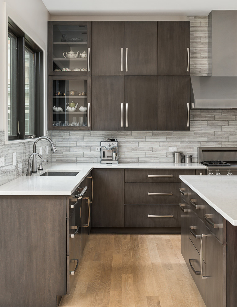 Photo of a large contemporary u-shaped open plan kitchen in Chicago with a submerged sink, flat-panel cabinets, quartz worktops, grey splashback, glass tiled splashback, stainless steel appliances, light hardwood flooring, an island, white worktops, dark wood cabinets and beige floors.