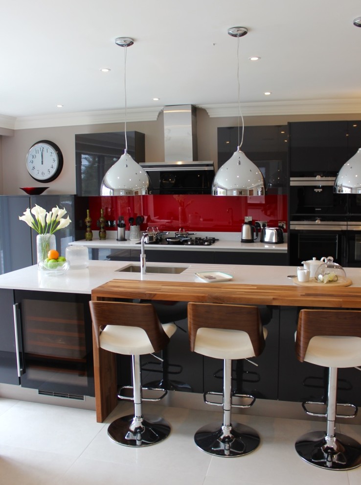 Große, Einzeilige Moderne Wohnküche mit flächenbündigen Schrankfronten, grauen Schränken, Küchenrückwand in Rot, Küchengeräten aus Edelstahl, Kücheninsel, Einbauwaschbecken, Quarzit-Arbeitsplatte, Glasrückwand und Porzellan-Bodenfliesen in Buckinghamshire