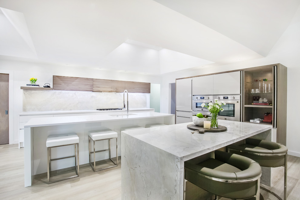 Photo of a large contemporary kitchen in Dallas with flat-panel cabinets, marble worktops, marble splashback, stainless steel appliances, light hardwood flooring, multiple islands, beige floors, a single-bowl sink and white splashback.