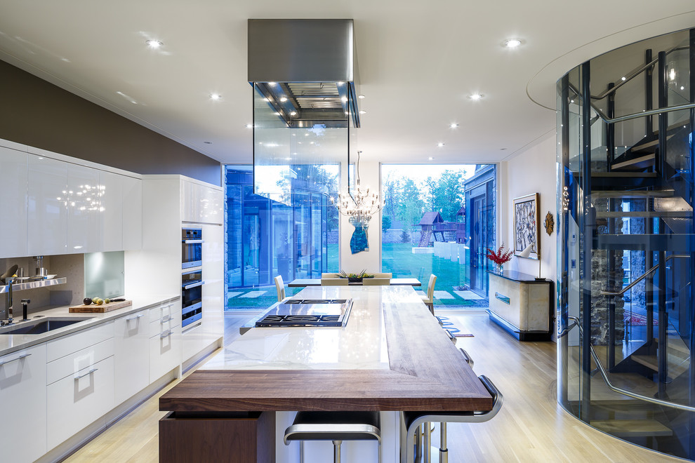Inspiration for a large contemporary galley light wood floor eat-in kitchen remodel in Ottawa with an undermount sink, flat-panel cabinets, white cabinets, wood countertops, gray backsplash, stone slab backsplash, stainless steel appliances and an island