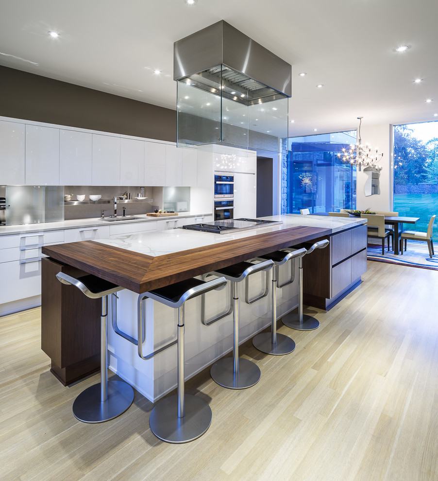 Inspiration for a large contemporary galley kitchen/diner in Ottawa with a submerged sink, flat-panel cabinets, white cabinets, wood worktops, grey splashback, stone slab splashback, stainless steel appliances, light hardwood flooring, an island and beige floors.