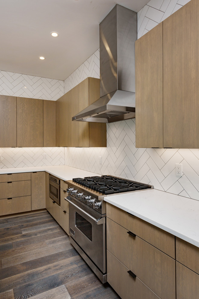 Diseño de cocina actual con salpicadero blanco, salpicadero de azulejos tipo metro, electrodomésticos de acero inoxidable, suelo de madera oscura, una isla y suelo gris