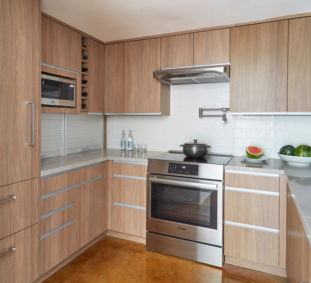 Foto på ett funkis grå u-kök, med släta luckor, skåp i mellenmörkt trä, vitt stänkskydd, rostfria vitvaror, betonggolv och brunt golv