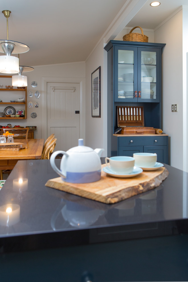 Inspiration for a small eclectic l-shaped kitchen/diner in Wellington with a double-bowl sink, open cabinets, stainless steel worktops, white splashback, ceramic splashback, stainless steel appliances, concrete flooring and an island.