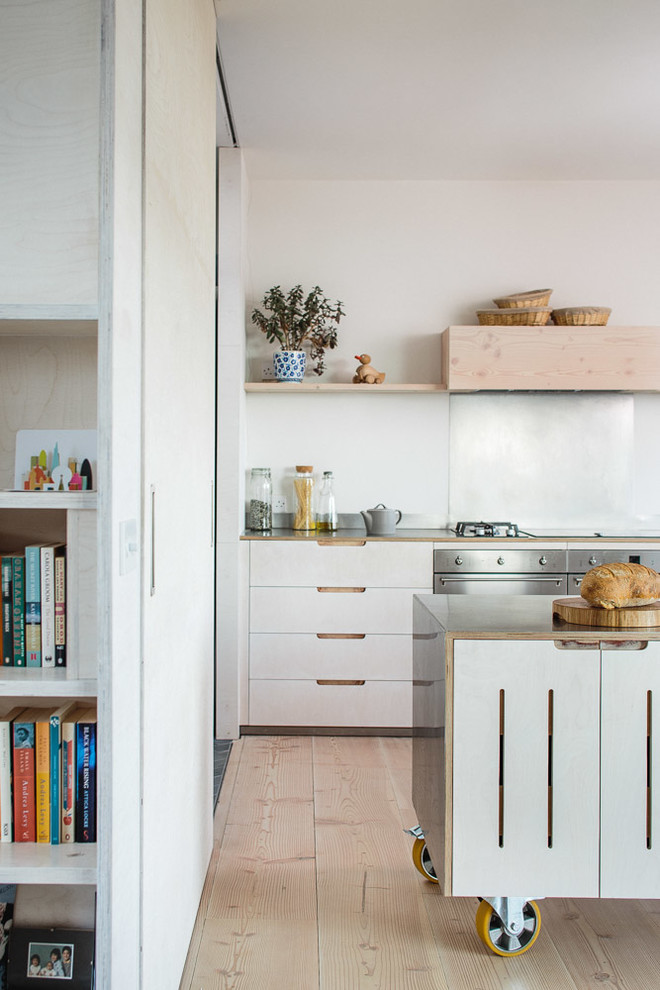 This is an example of a medium sized scandinavian l-shaped kitchen/diner in Other with a belfast sink, flat-panel cabinets, light wood cabinets, stainless steel worktops, metallic splashback, stainless steel appliances, light hardwood flooring and an island.