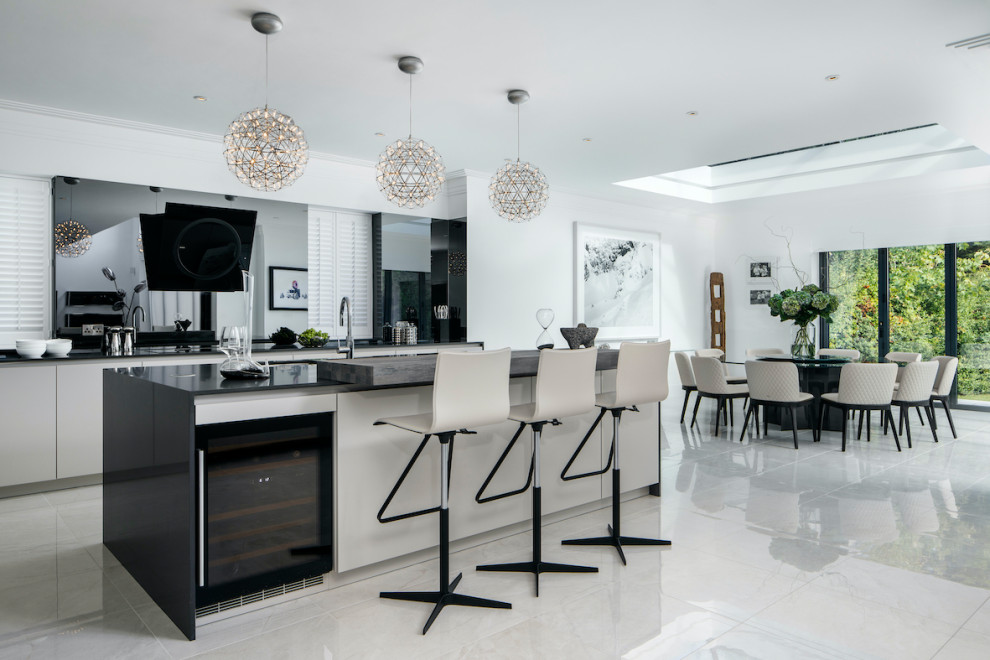 This is an example of a large contemporary l-shaped open plan kitchen in Essex with flat-panel cabinets, beige cabinets, black splashback, integrated appliances, marble flooring, an island, black worktops and white floors.