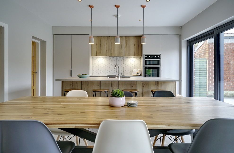 This is an example of a medium sized contemporary single-wall open plan kitchen in Belfast with a built-in sink, flat-panel cabinets, beige cabinets, laminate countertops, white splashback, ceramic splashback, black appliances, cement flooring, an island, grey floors and grey worktops.