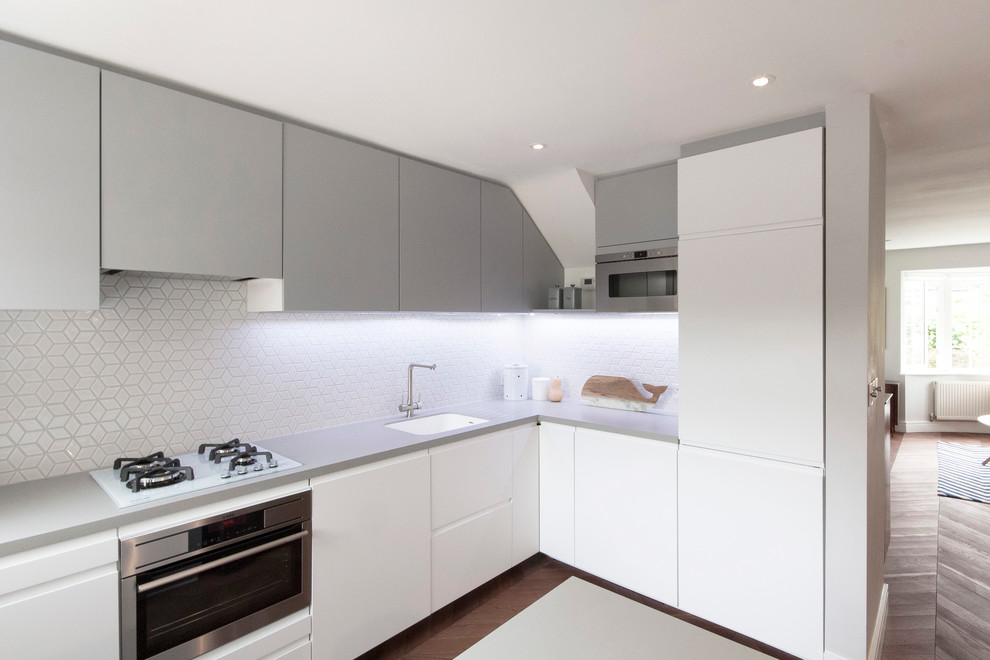 Inspiration for a small scandinavian l-shaped open plan kitchen in London with a built-in sink, flat-panel cabinets, white cabinets, composite countertops, white splashback, mosaic tiled splashback, stainless steel appliances, dark hardwood flooring and an island.