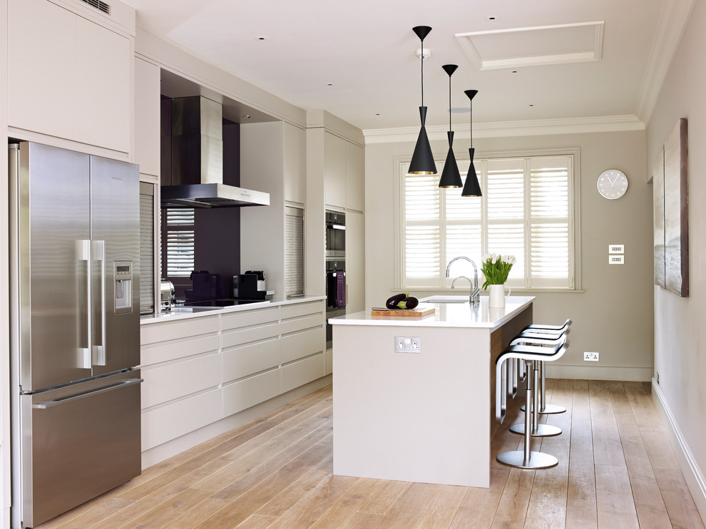 Foto di una cucina minimal di medie dimensioni con ante lisce, ante grigie, paraspruzzi con lastra di vetro, elettrodomestici in acciaio inossidabile e pavimento in legno massello medio
